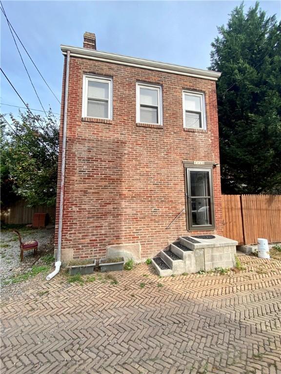 view of front facade with brick siding, a chimney, a patio area, and fence