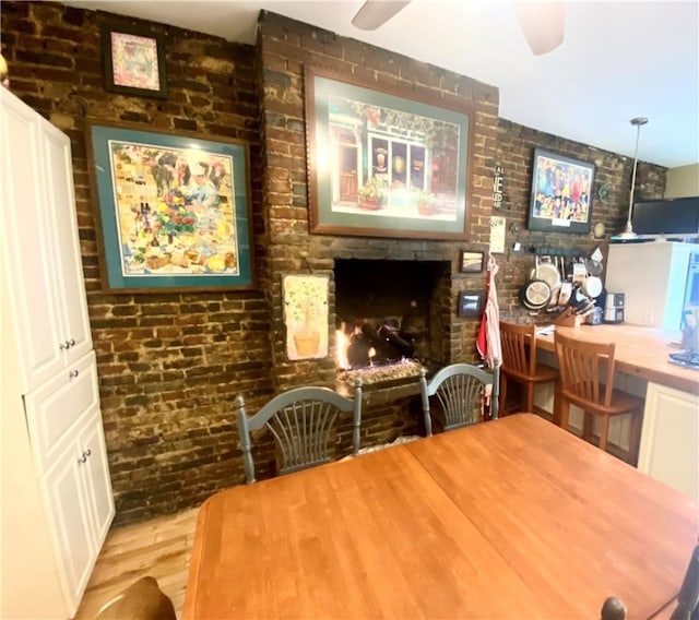 dining space featuring brick wall, a fireplace, a ceiling fan, and wood finished floors