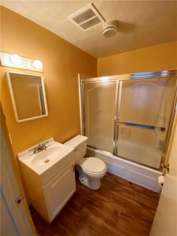 full bath featuring toilet, bath / shower combo with glass door, wood finished floors, vanity, and visible vents