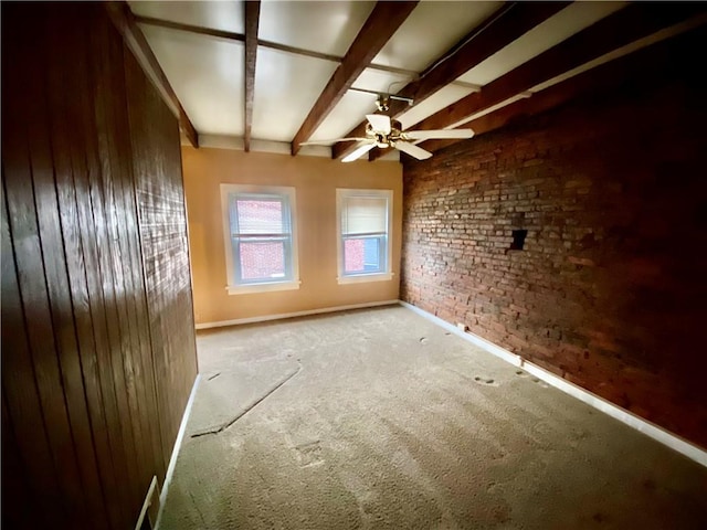 unfurnished room with brick wall, carpet flooring, a ceiling fan, baseboards, and beam ceiling