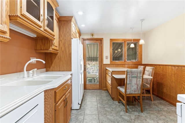 kitchen featuring light tile patterned flooring, sink, decorative light fixtures, white appliances, and wooden walls