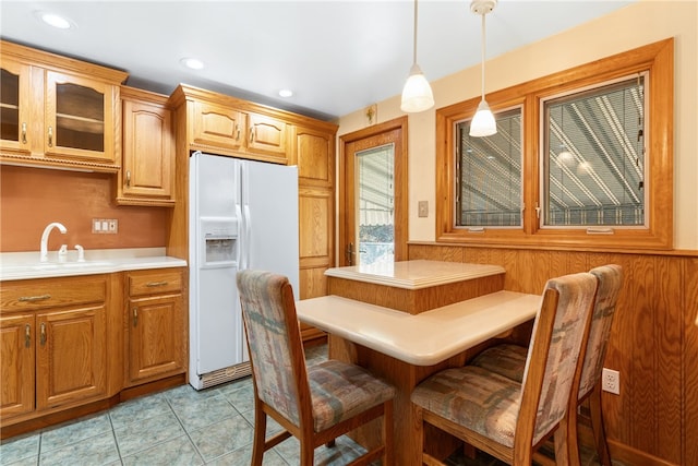 kitchen featuring a kitchen bar, light tile patterned floors, white fridge with ice dispenser, hanging light fixtures, and sink