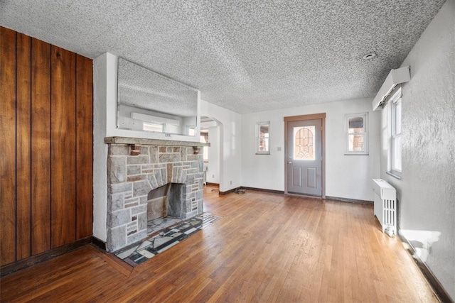 unfurnished living room featuring hardwood / wood-style flooring, a stone fireplace, a textured ceiling, and radiator heating unit