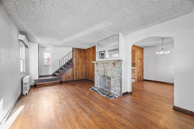 unfurnished living room featuring radiator heating unit, wood-type flooring, a fireplace, a textured ceiling, and a notable chandelier