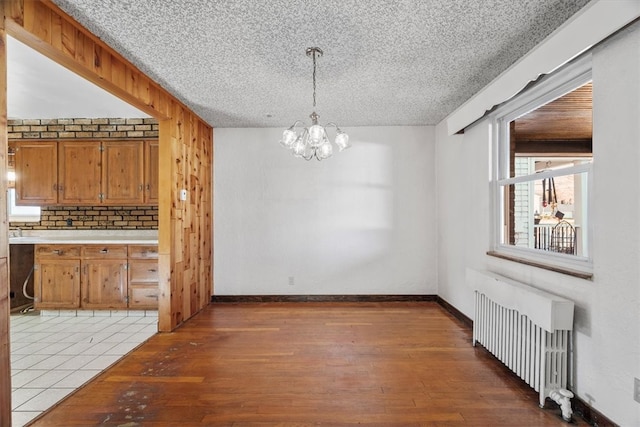 unfurnished dining area with radiator heating unit, wood walls, a textured ceiling, hardwood / wood-style flooring, and a chandelier