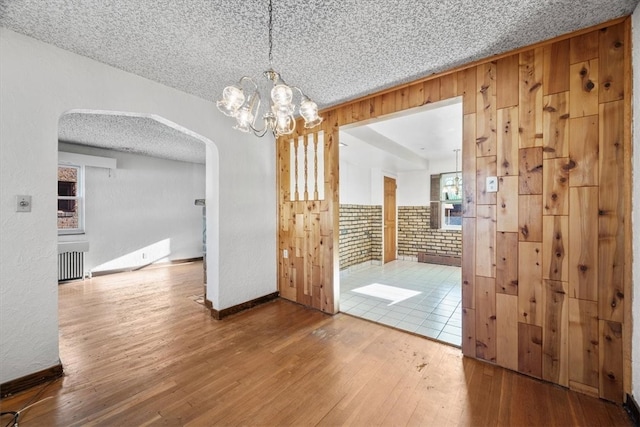 interior space featuring brick wall, radiator, a textured ceiling, hardwood / wood-style floors, and a notable chandelier