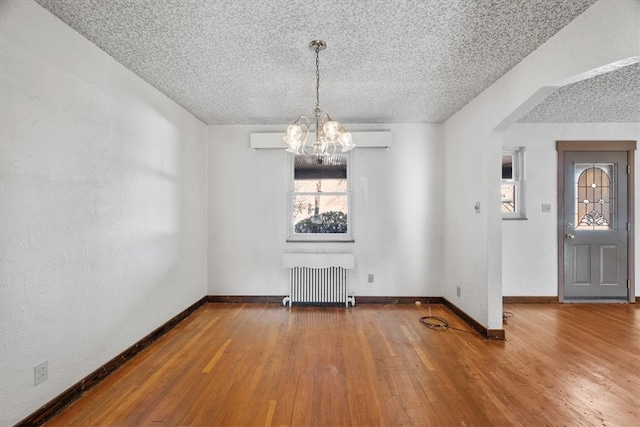 unfurnished dining area with wood-type flooring, a textured ceiling, a chandelier, and radiator