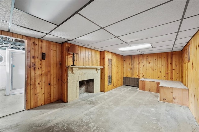 basement with a drop ceiling, a fireplace, and wooden walls