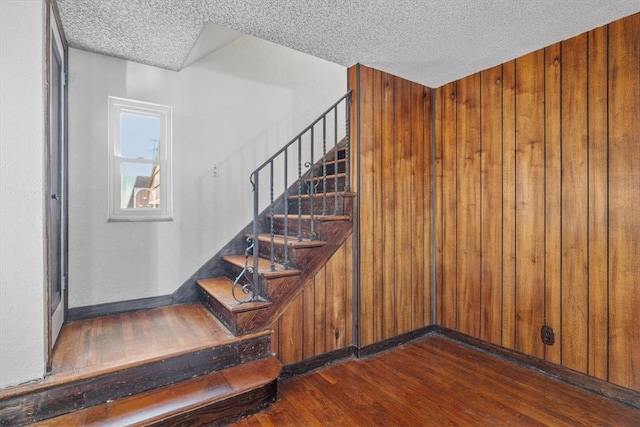 stairway featuring wooden walls, hardwood / wood-style floors, and a textured ceiling