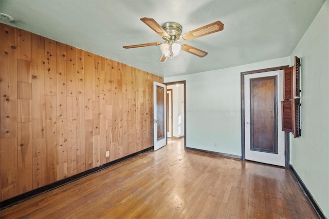 spare room with ceiling fan, wooden walls, and light wood-type flooring