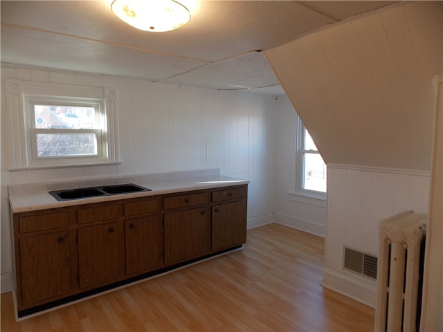 kitchen featuring light hardwood / wood-style flooring, radiator, wooden walls, and sink