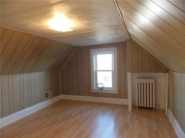 additional living space featuring radiator heating unit, wood walls, vaulted ceiling, and light hardwood / wood-style floors