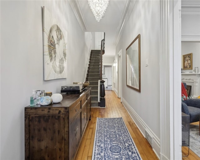 hall with a notable chandelier, ornamental molding, and light hardwood / wood-style flooring