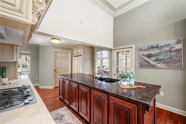 kitchen with high end refrigerator, sink, hardwood / wood-style flooring, stainless steel gas stovetop, and an island with sink