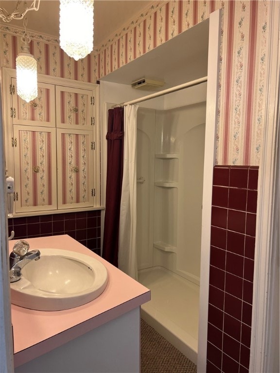 bathroom with a shower with curtain, vanity, an inviting chandelier, and tile walls