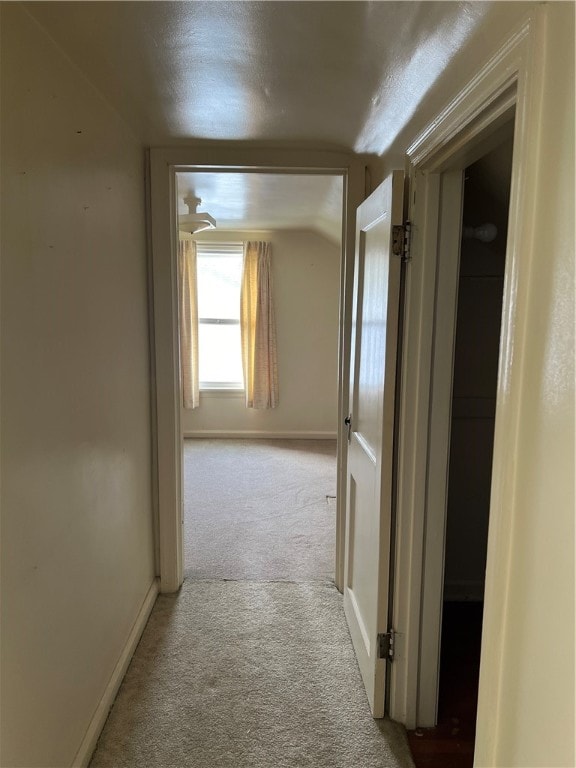 hall featuring a textured ceiling, light colored carpet, and lofted ceiling