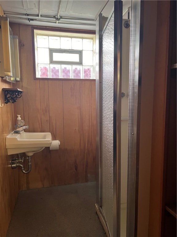 bathroom featuring wood walls, a shower with shower door, and sink