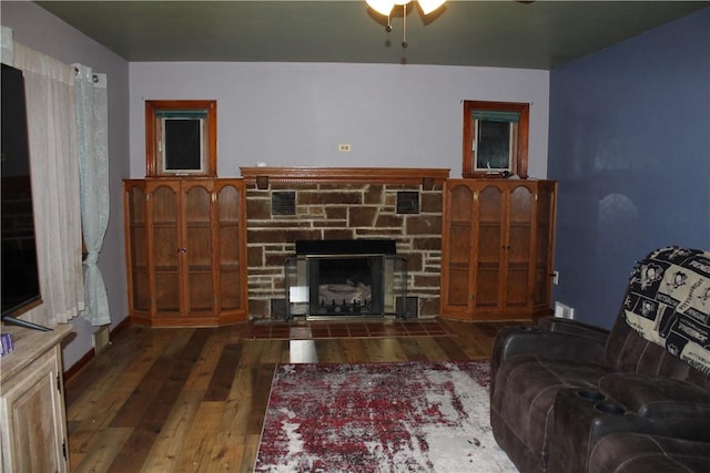 living room with dark hardwood / wood-style floors, ceiling fan, and a stone fireplace