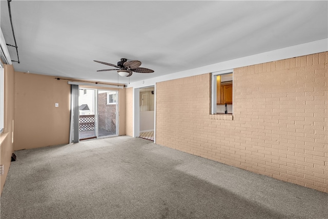 carpeted spare room featuring ceiling fan and brick wall