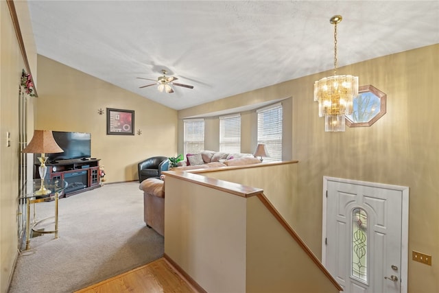 living room with ceiling fan with notable chandelier, vaulted ceiling, and light hardwood / wood-style flooring