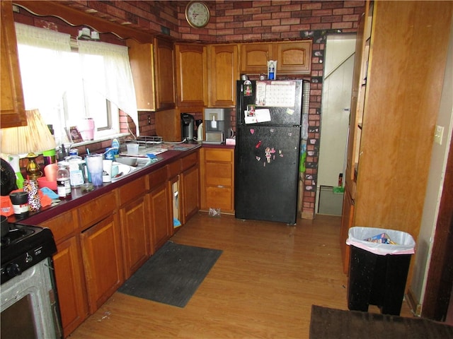 kitchen featuring black appliances, light hardwood / wood-style floors, and brick wall