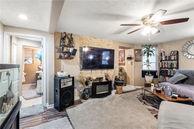 living room featuring a stone fireplace, hardwood / wood-style floors, a textured ceiling, and ceiling fan