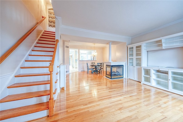 interior space with a multi sided fireplace, hardwood / wood-style floors, an inviting chandelier, and crown molding