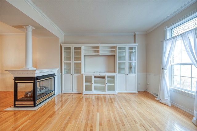 unfurnished living room with a multi sided fireplace, ornate columns, a healthy amount of sunlight, and light wood-type flooring