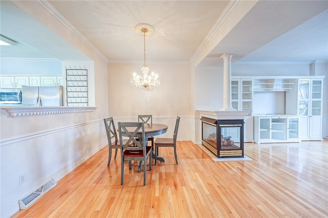 dining area featuring a multi sided fireplace, decorative columns, crown molding, a chandelier, and light hardwood / wood-style floors