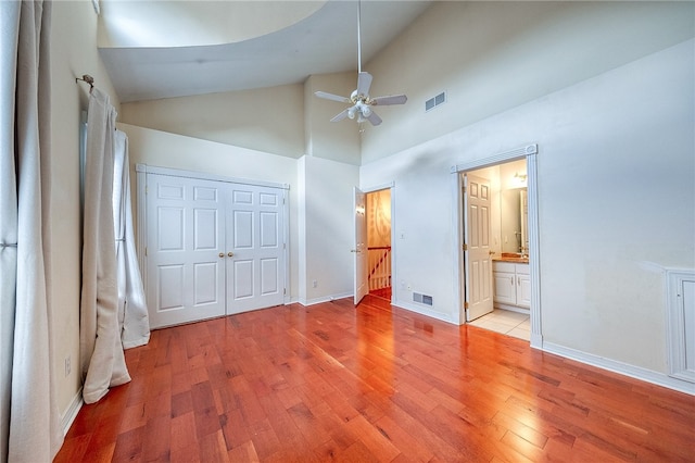 unfurnished bedroom with light wood-type flooring, high vaulted ceiling, ceiling fan, and connected bathroom