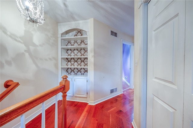 hall featuring hardwood / wood-style floors, a textured ceiling, and a notable chandelier