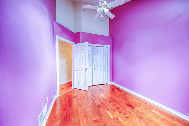 unfurnished bedroom featuring a high ceiling, a closet, light hardwood / wood-style floors, and ceiling fan