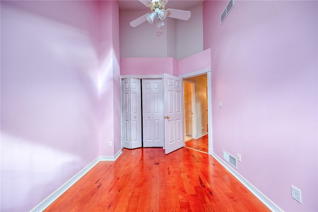 unfurnished bedroom with a high ceiling, a closet, light hardwood / wood-style floors, and ceiling fan