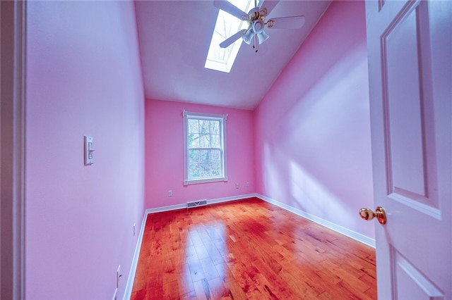 empty room featuring ceiling fan, vaulted ceiling with skylight, and light hardwood / wood-style floors