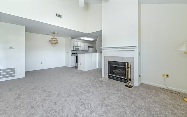 unfurnished living room featuring a high ceiling, a tiled fireplace, and light carpet