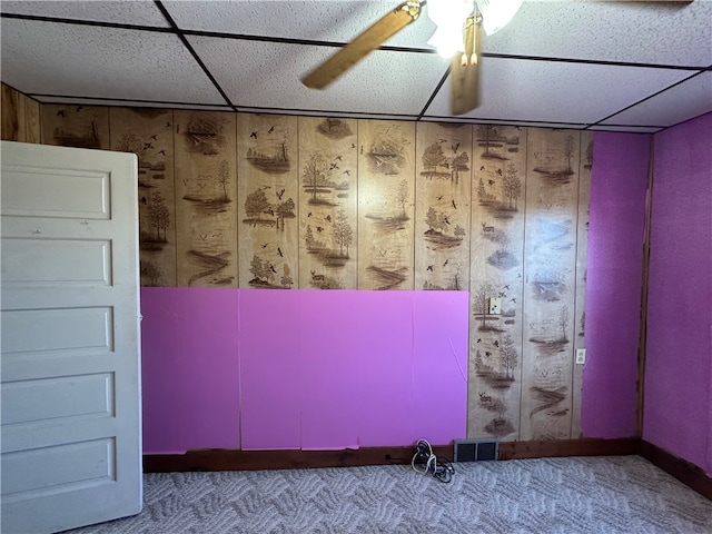 unfurnished room featuring ceiling fan, a drop ceiling, carpet floors, and wooden walls