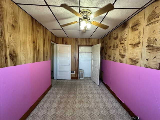 interior space featuring ceiling fan, wooden walls, and a drop ceiling