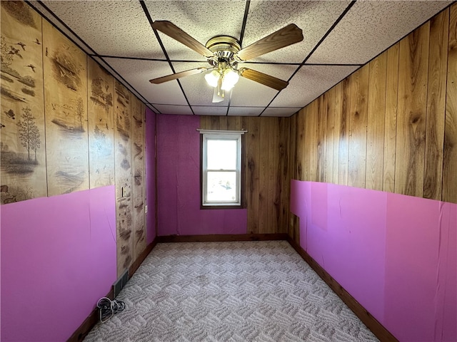 spare room with a drop ceiling, light colored carpet, ceiling fan, and wooden walls