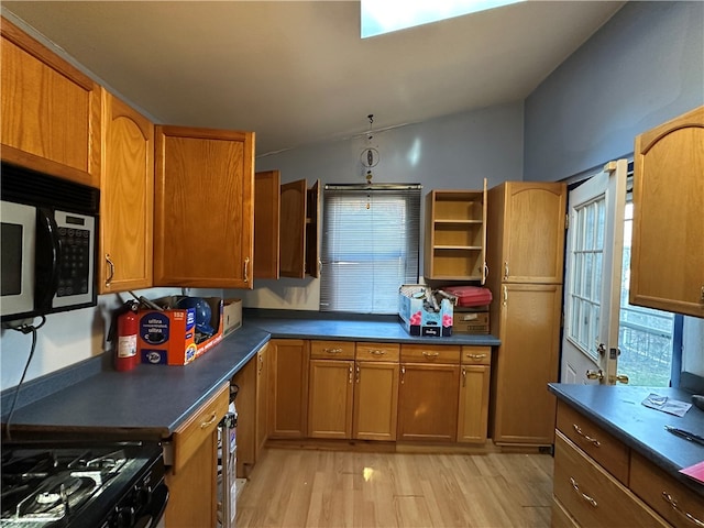 kitchen featuring vaulted ceiling with skylight, plenty of natural light, light wood-type flooring, and black range