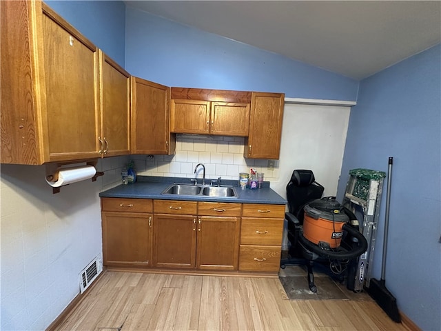 kitchen featuring decorative backsplash, light hardwood / wood-style floors, sink, and vaulted ceiling