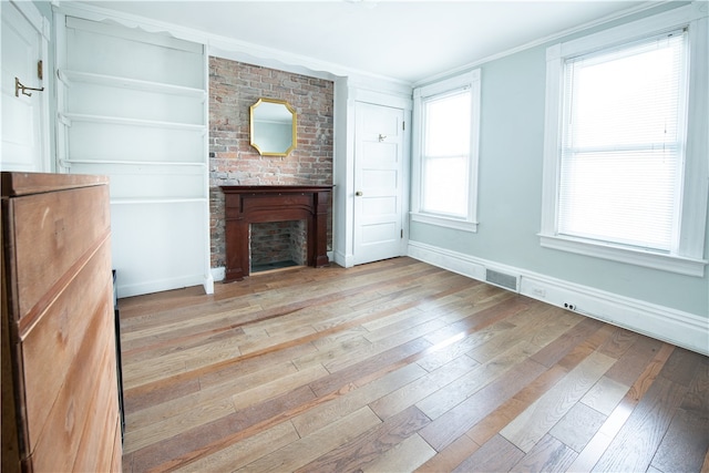 unfurnished living room featuring light wood-type flooring, a brick fireplace, and a healthy amount of sunlight