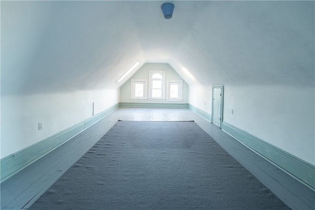 additional living space featuring wood walls, lofted ceiling, and carpet flooring