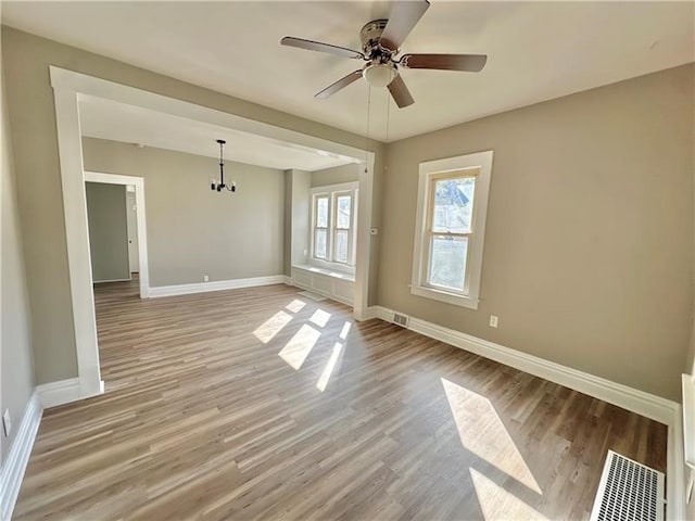 unfurnished room featuring ceiling fan with notable chandelier and light hardwood / wood-style flooring