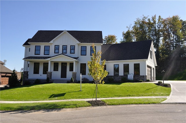 view of front facade featuring a shingled roof, concrete driveway, a standing seam roof, board and batten siding, and a front yard