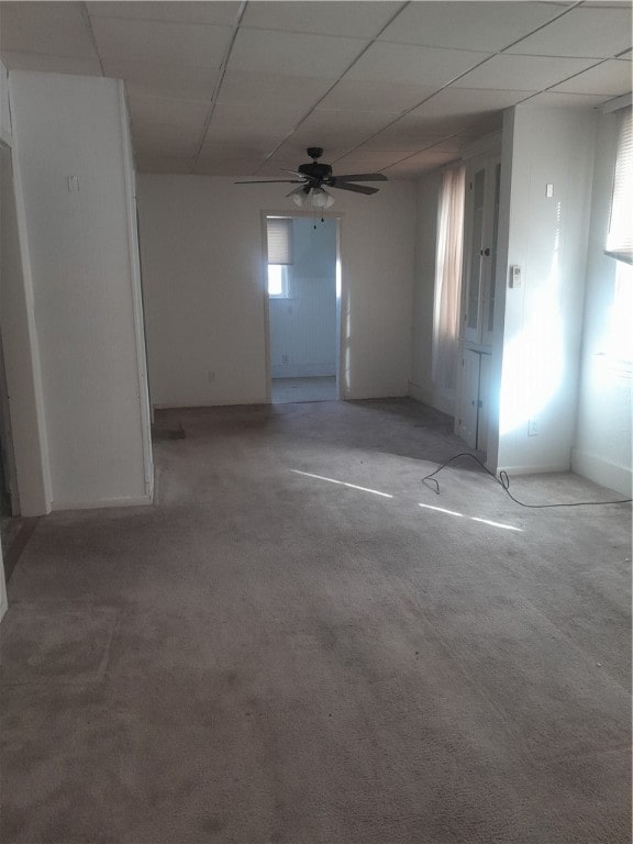 carpeted spare room featuring ceiling fan, a drop ceiling, and a healthy amount of sunlight