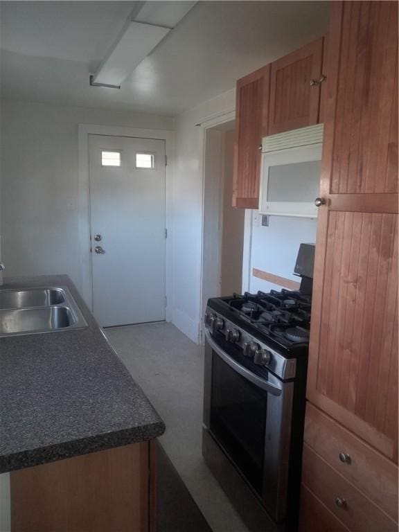 kitchen with gas stove, white microwave, dark countertops, brown cabinets, and a sink