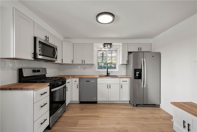 kitchen featuring backsplash, white cabinets, light wood-type flooring, appliances with stainless steel finishes, and butcher block countertops