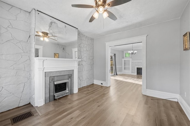 unfurnished living room with a textured ceiling, ceiling fan with notable chandelier, a fireplace, and hardwood / wood-style flooring