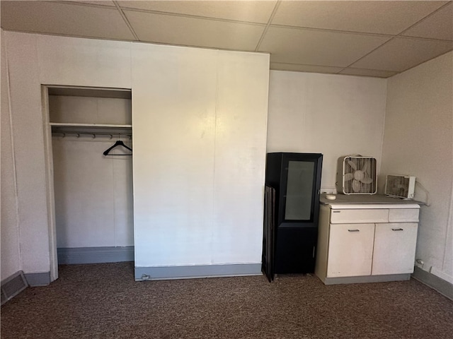 interior space with a paneled ceiling, a closet, and dark colored carpet