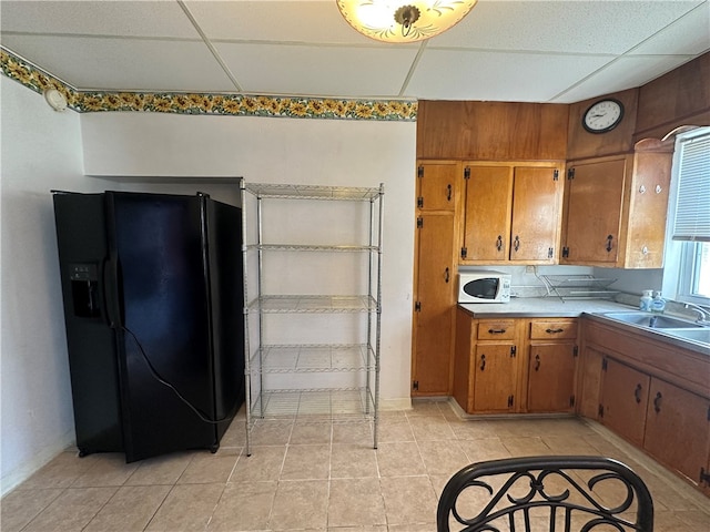 kitchen featuring black fridge with ice dispenser, a drop ceiling, light tile patterned floors, and sink